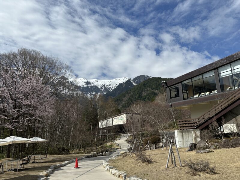 しらかば平駅の建物と桜、雪をかぶった北アルプス（春・4月）